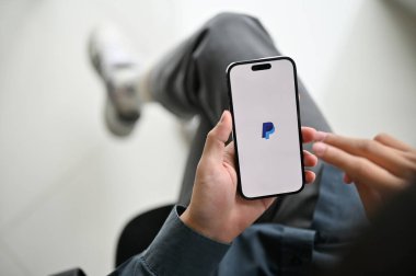 Chiang Mai, Thailand - Feb 17 2023: close-up image of an Asian man using PayPal mobile application to pay his bills. iPhone with PayPal logo on screen.