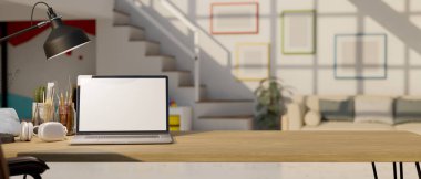 close-up, Workspace with laptop white screen mockup, headphones, painting tools, table lamp and copy space on wood tabletop over blurred background of minimal living room. 3d render, 3d illustration