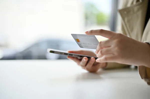 Close-up side view image of a woman\'s hands holding a smartphone and a credit card at the table. mobile banking, online shopping, e-commerce business