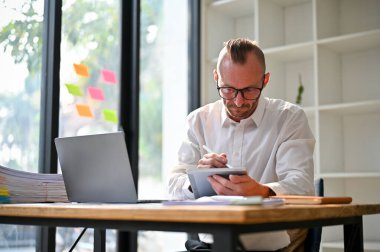 Determined and professional caucasian male boss or businessman working on his business tasks on tablet at his desk in the office.