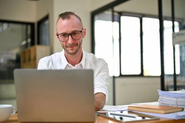 Smart and professional Caucasian businessman using laptop computer at his desk, working in the office.