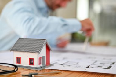 Close-up image of a beautiful house model is on the table over blurred background or professional male engineer working on a blueprint.