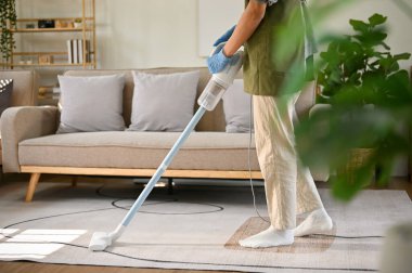 Cropped image of a man wearing rubber gloves and using stick vacuum cleaner to clean the carpet in his minimal living room. house cleaning concept. side view