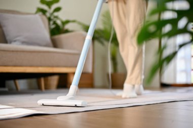 Cropped image of a man using stick vacuum cleaner to clean the carpet in his minimal living room. house chores, housekeeping, big cleaning day