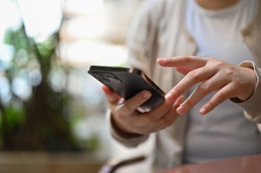 Close-up image of an Asian woman chatting with her friends through her smartphone, using her phone while relaxing in the backyard.
