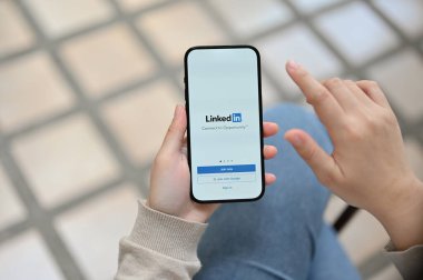 Chiang Mai, Thailand - Feb 23 2023: A woman's hand holding a smartphone with LinkedIn logo on screen. iPhone with LinkedIn logo. online resume, job, career