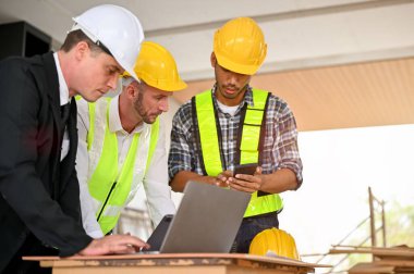 Professional caucasian male construction engineer manager working with an Asian foreman and a Caucasian businessman at the construction site. Diverse workers concept