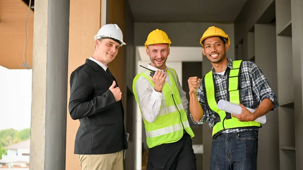 Teamwork and diverse workers concept, Cheerful Asian construction worker, Caucasian businessman and foreman showing fist, smiling, looking at camera, celebrating success work together in the site.