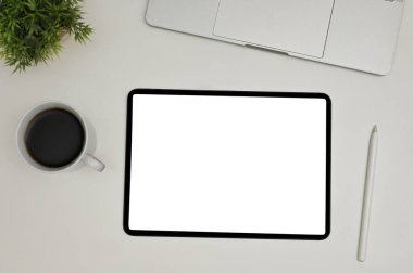 Top view of a modern workspace with digital tablet touchpad white screen mockup, stylus pen, laptop, coffee cup and decor plant on white background.
