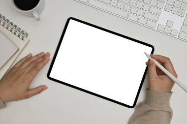 Top view, A female writing on digital tablet at her minimal working desk, tablet white screen mockup.