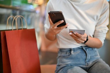 Cropped image of a woman holding a credit card and using her smartphone to register an online shopping app or check shopping points while shopping at the mall.