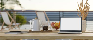 Laptop white screen mockup, tea set, book, pampas grass in a ceramic vase, and apple bowl on minimal wood table over blurred outdoor relaxation space in background. 3d render, 3d illustration