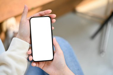 Top view of a modern smartphone white screen mockup is in a woman's hands over blurred background.