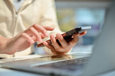 Cropped shot of an Asian woman in casual clothes using her smartphone to communicate with her coworker while remote working at the cafe. text, chat, message, email