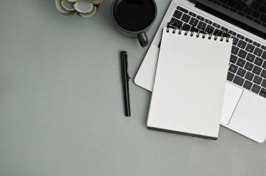 Modern office desk workspace top view with laptop, pen, coffee cup, decor plant, blank spiral notepad and space on grey background.