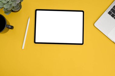 Overhead view of yellow workspace with digital tablet white screen mockup with accessories.
