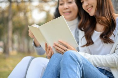 Güzel yeşil parktaki ağacın altında büyükannesiyle kitap okuyan mutlu ve sevimli bir Asyalı torunun görüntüsü..