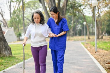 Mutlu ve gülümseyen, engelli, bastonlu Asyalı kadın parkta dinlenirken bakıcısıyla konuşmaktan zevk alıyor..