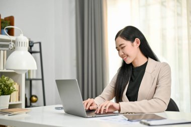 Güzel ve zarif Asyalı iş kadını ya da resmi takım elbiseli kadın CEO 'nun ofis masasındaki görevleri üzerinde çalışırken dizüstü bilgisayar kullanışının yan görüntüsü..