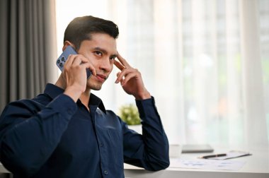 Ciddi ve düşünceli Asyalı iş adamı ya da erkek patron müşterisiyle ofiste ciddi bir telefon görüşmesi yapıyor..