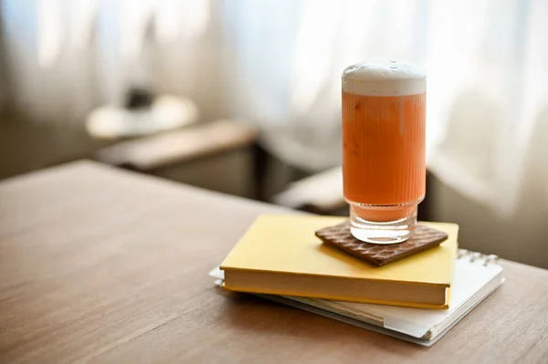A glass of iced Thai tea is on a book on a wooden table in the minimalist cafe. drinks concept