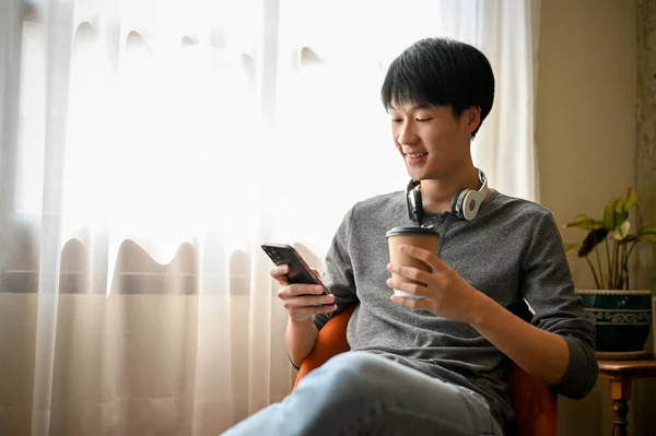 stock image Happy and handsome young Asian man in trendy clothes using his phone while sipping coffee in the coffee shop.