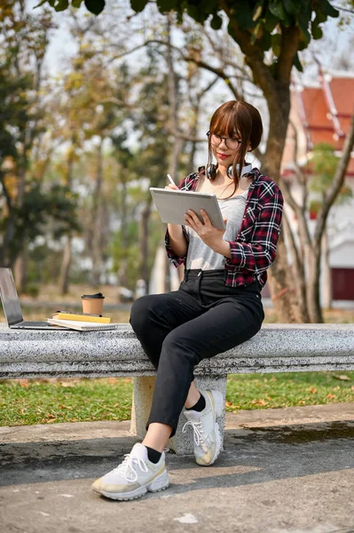 穿着休闲装的年轻亚洲女大学生的画像坐在长椅上 用她的便携式数码平板电脑 — 图库照片