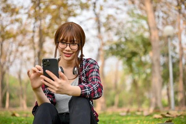 Yeşil Parkta Çimde Otururken Telefonuyla Günlük Kıyafetlerini Giyen Güzel Genç — Stok fotoğraf