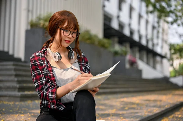 キャンパスの建物の外の階段に座って何かを書くか 彼女の本の中で通りの景色をスケッチ — ストック写真