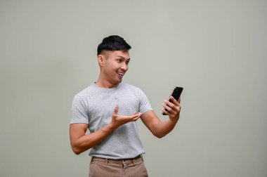 Mutlu ve neşeli bin yıllık Asyalı adam telefonunun ekranına bakıyor. Çevrimiçi bir alışveriş uygulamasında online satış promosyonuyla, yeşil bir stüdyonun arka planında duruyor..