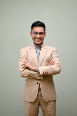 Milenyum Asyalı akıllı ve kendinden emin iş adamı ya da resmi iş elbisesi giymiş erkek yönetici kolları bağlı yeşil bir stüdyoya karşı duruyor..