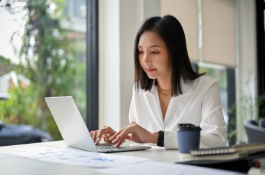 Odaklanmış ve profesyonel Asyalı iş kadını laptopunu kullanıyor, iş görevleri üzerinde çalışıyor ofisi iyon.