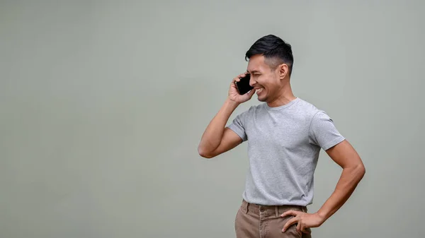 身穿休闲装 面带笑容 快乐的亚洲男人 把目光投向一边 与人通电话 面对着一个空荡荡的绿色工作室背景 展示你的文字 — 图库照片