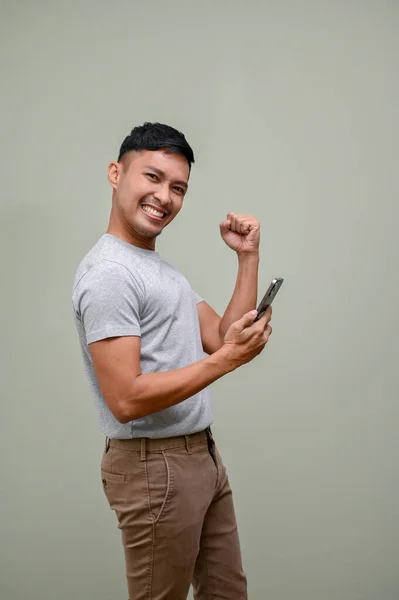 兴奋的身穿休闲装的千禧年亚洲男人举着手机 是的手势 庆祝好消息 孤立的绿色背景 — 图库照片