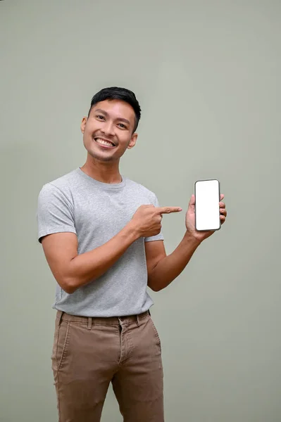 快乐而又面带微笑的千年亚洲人将手指指向手中的智能手机屏幕 电话白屏模拟 孤立的背景 — 图库照片
