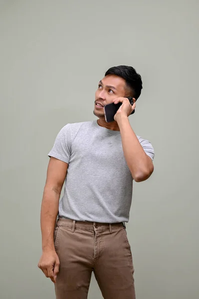 困惑的身穿休闲装的千禧年亚洲男人 一边站在孤立的绿色背景下 一边看一边抬头 与人通电话 — 图库照片