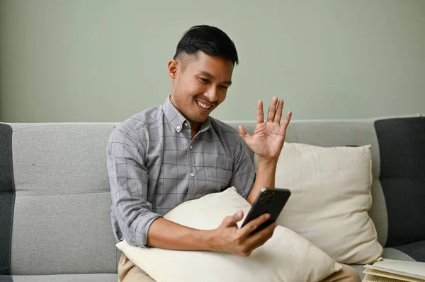 身穿休闲装的快乐的千年亚洲男人在客厅里和他的朋友通过视频交谈 — 图库照片