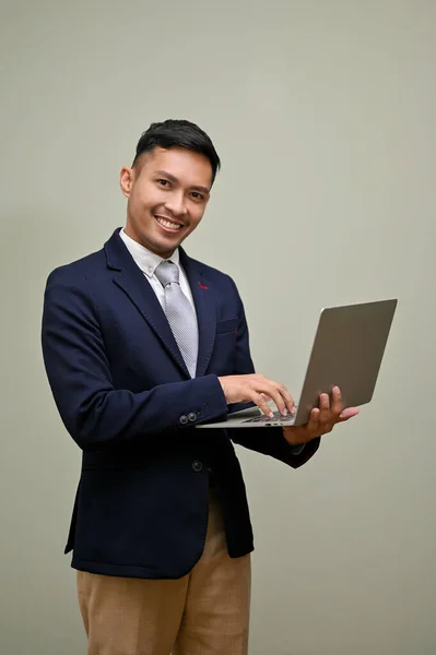 穿着正式西装的成功而英俊的千年亚洲商人 手持手提电脑 使用笔记本电脑 一边在键盘上打字 一边站在孤立的绿色背景下 — 图库照片