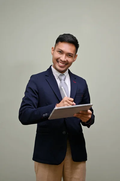 stock image Portrait, Smiling and happy millennial Asian businessmen in formal business suit using his digital tablet and looking at the camera while standing against an isolated green background.