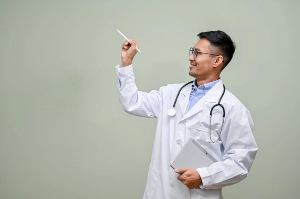 彼のポータブルタブレットと聴診器と白いガウンを着たアジアの男性医師は 緑の背景に隔離された空の空間でペンを指しています — ストック写真