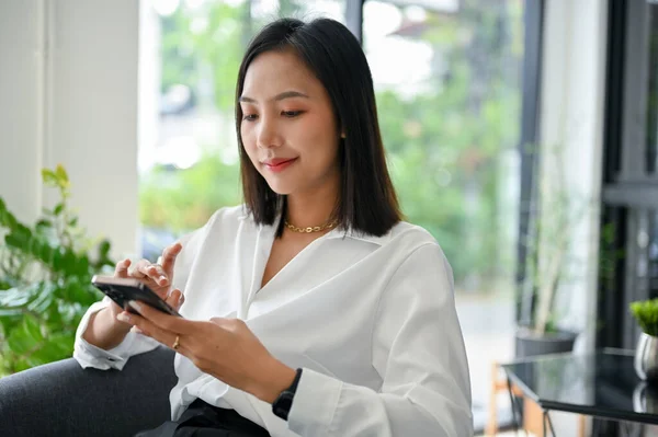 美丽而快乐的千年亚洲女商人或女执行经理在办公室放松的时候用手机 — 图库照片