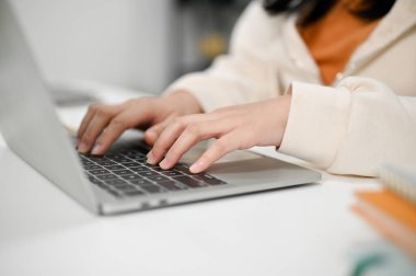 Günlük giysiler içinde Asyalı bir kadının, işini yönetmek için bilgisayarını kullanırken, klavyede yazarken, internette gezinirken çekilmiş görüntüsü..