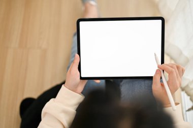 Asyalı bir kadının oturma odasında dijital tabletini kullanışının en üst görüntüsü. Grafik reklamlarınızı göstermek için tablet beyaz ekran modellemesi.