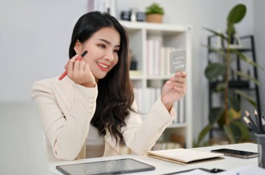 Çekici ve güzel Asyalı bayan ofis çalışanı ofisteki masasına makyaj yapıyor..