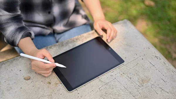 an Asian woman in flannel shirt using her digital tablet at the green park. people and technology concept. close-up image