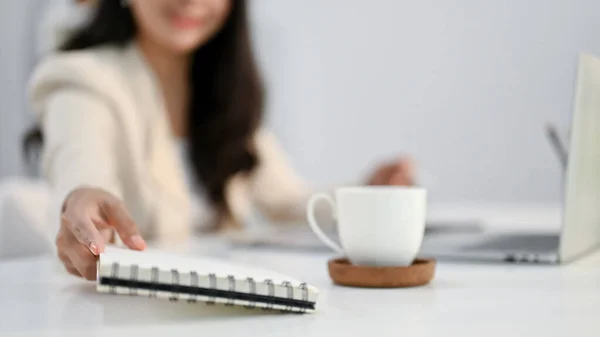 stock image Close-up image of a businesswoman or female office worker grabbing a spiral notepad, working on her tasks at her desk.