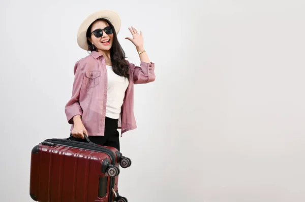 迷人而快乐的年轻亚洲女性游客 头戴草帽 戴着太阳镜 背着行李 站在孤立的白色背景下挥手 — 图库照片