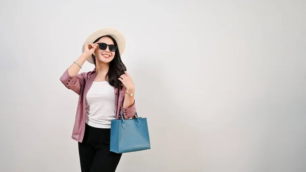 stock image Attractive and beautiful young Asian female tourist or shopper wearing sunglasses and a straw hat stands against an isolated white background with empty space for displaying your text.