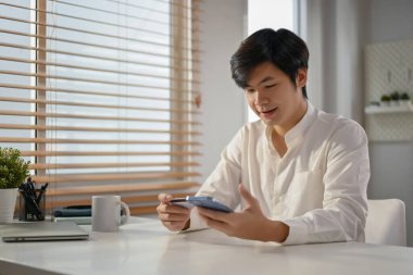 Mutlu Asyalı adam cep telefonu bankacılığı uygulamasını kullanarak para aktarıyor ya da online alışveriş faturalarını ödüyor. finansal ve teknoloji kavramı