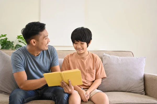 Happy and kind Asian dad is talking and telling a story to his son on a sofa in the living room. family happy time concept